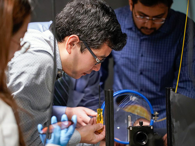 Xingjie Ni (center) manipulates a conventional telescope lens.